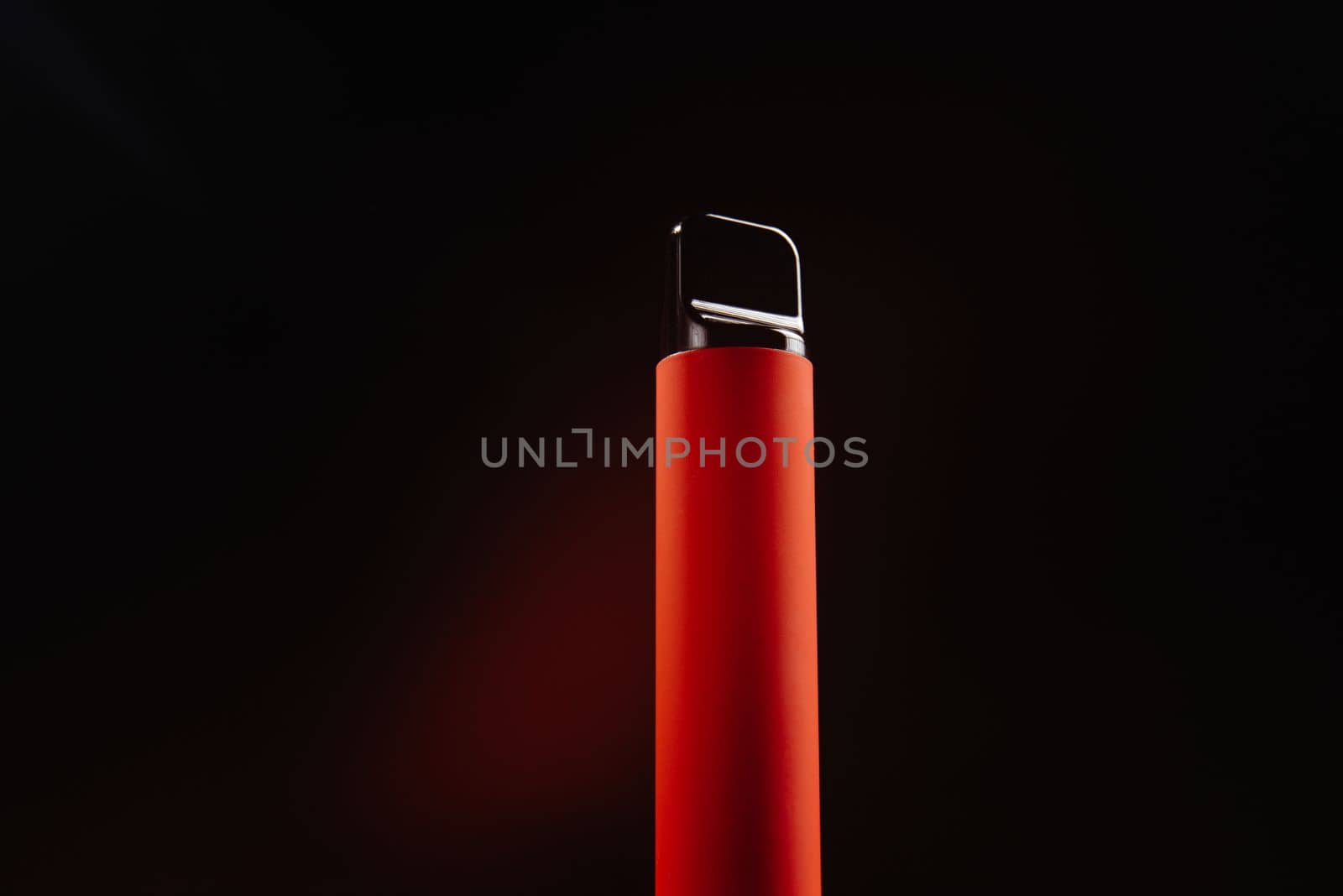 Red disposable e-cigarette on a dark background. Electronic vape, an alternative to smoking cigarettes. Colorful disposable electronic cigarette isolated on a white background. The concept of modern smoking, vaping and nicotine