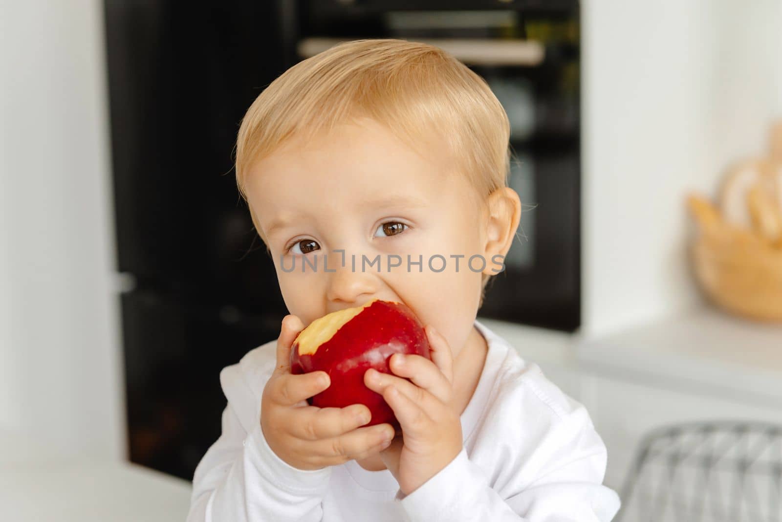 The child eats an apple for breakfast sitting in the kitchen. Healthy eating for the whole family. Reducetarian Eating Enjoying Plant-Based Food. by gulyaevstudio