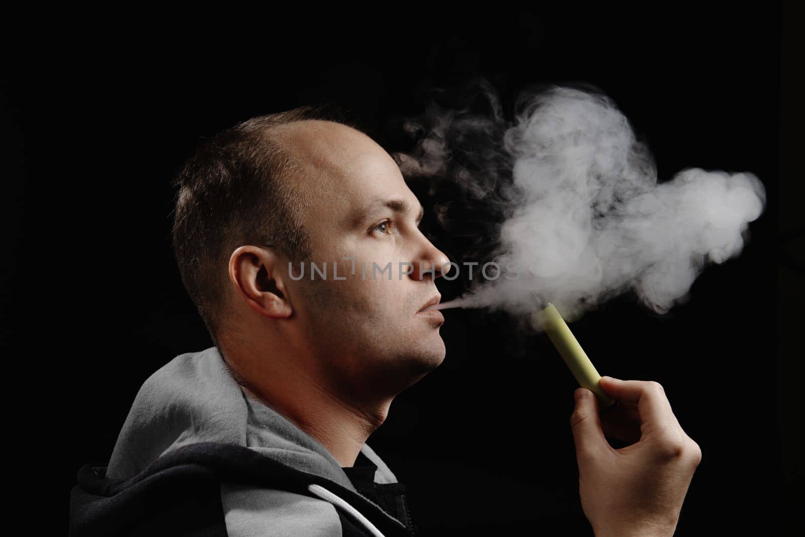 A man uses an electronic cigarette against a black background. Space for text. Alternative to smoking. How to quit smoking. by gulyaevstudio