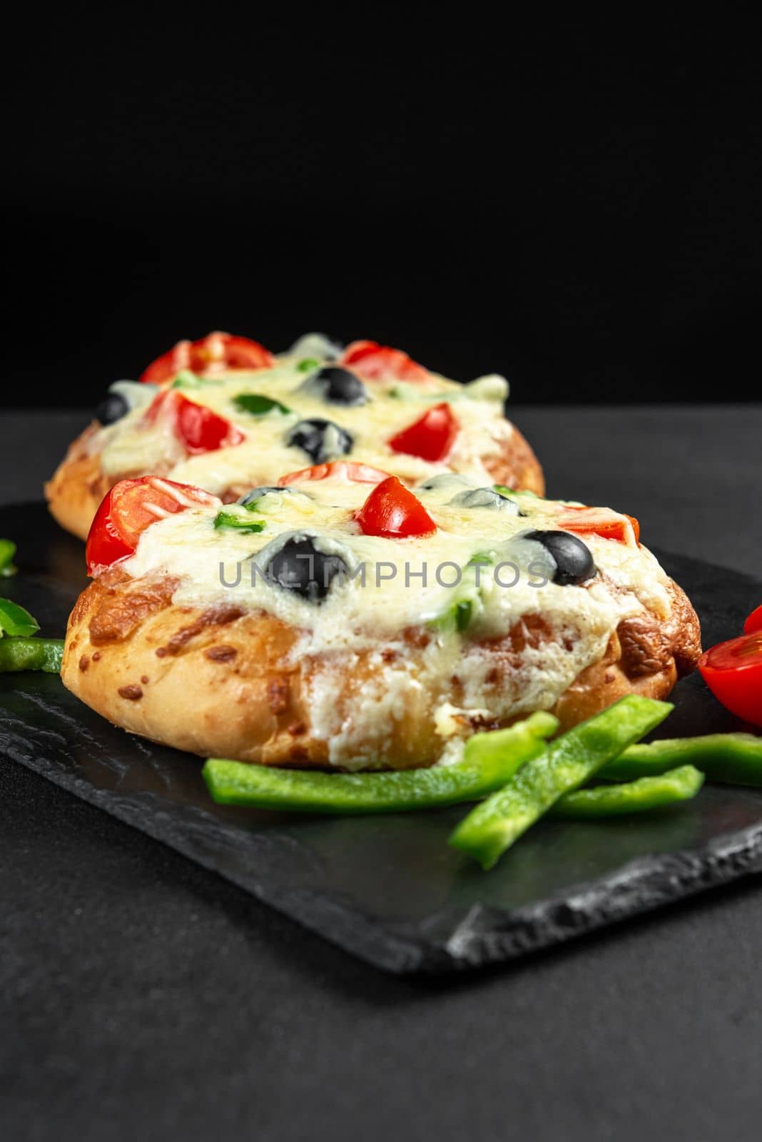 Homemade Indian pizza on small tortillas on a black background. Vertical Frame by gulyaevstudio