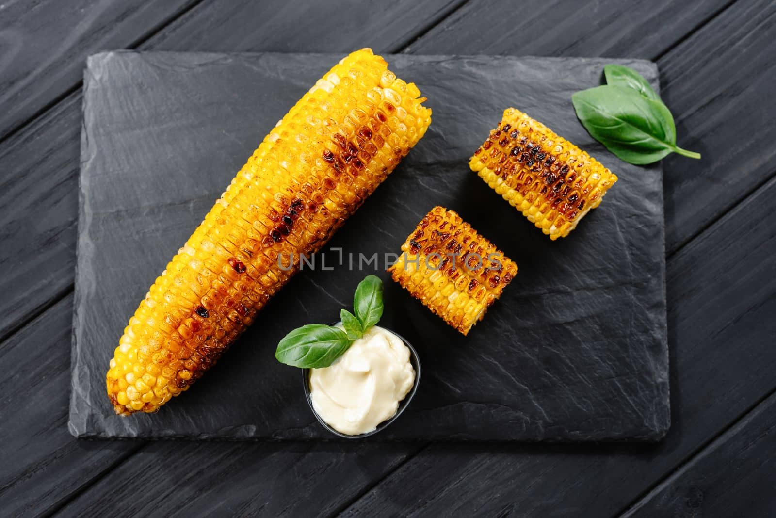 Grilled corn on a dark wooden background. Slices of sliced corn grilled on charcoal.
