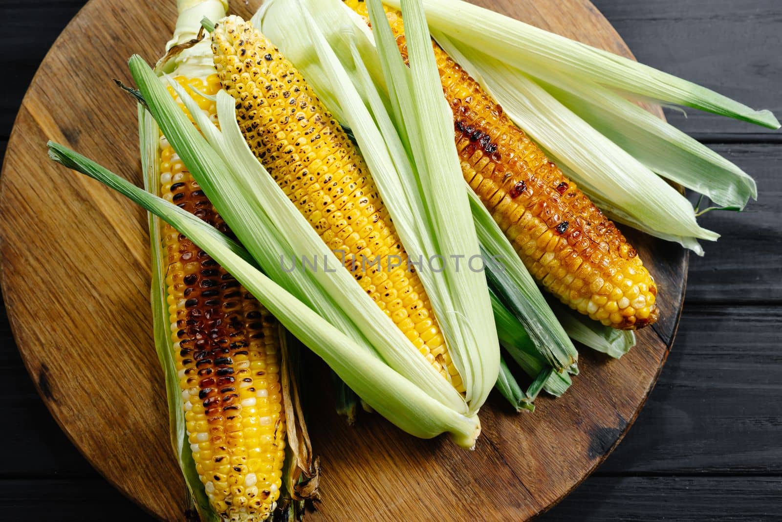 A cauldron of corn roasted over charcoal on a wooden board. Whole corn cobs.