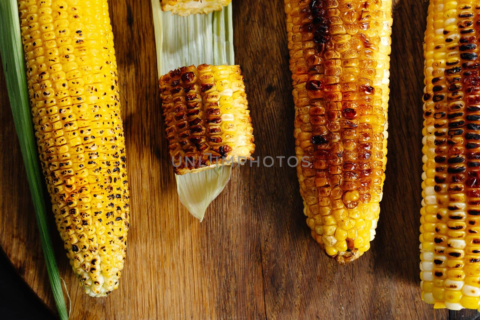 Roasted barbecue corn. Grilled corn on a dark wooden background. Slices of sliced corn grilled on charcoal. Top view by gulyaevstudio