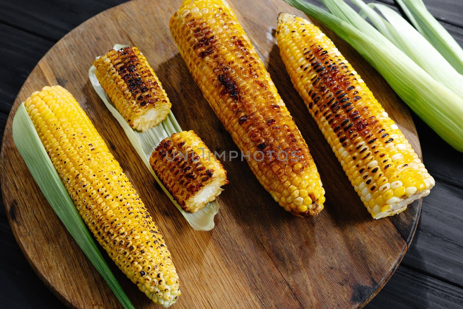 Roasted barbecue corn. Grilled corn on a dark wooden background. Slices of sliced corn grilled on charcoal. Top view.