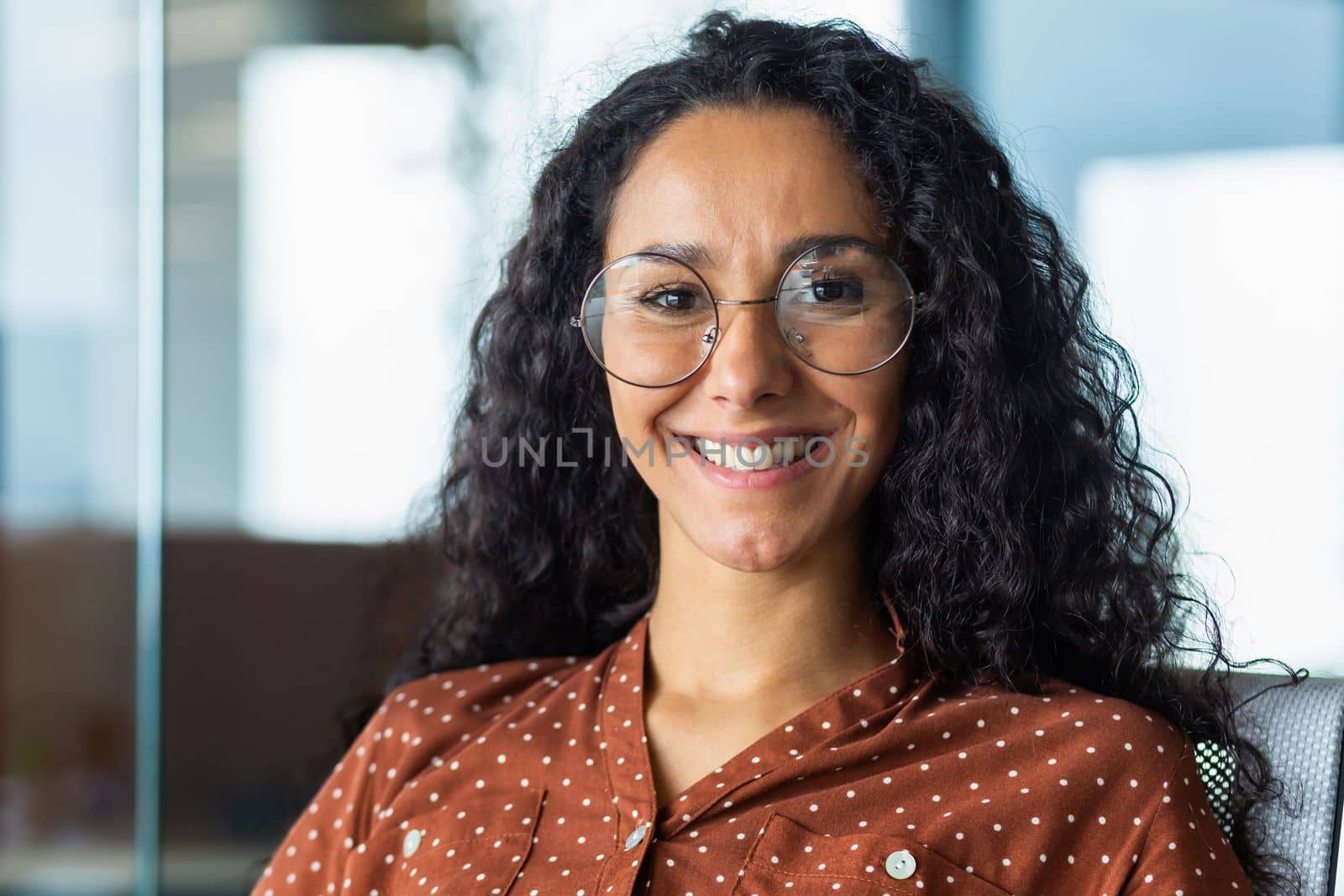 Close-up portrait of beautiful Latin American businesswoman smiling and looking at camera, working inside modern office.