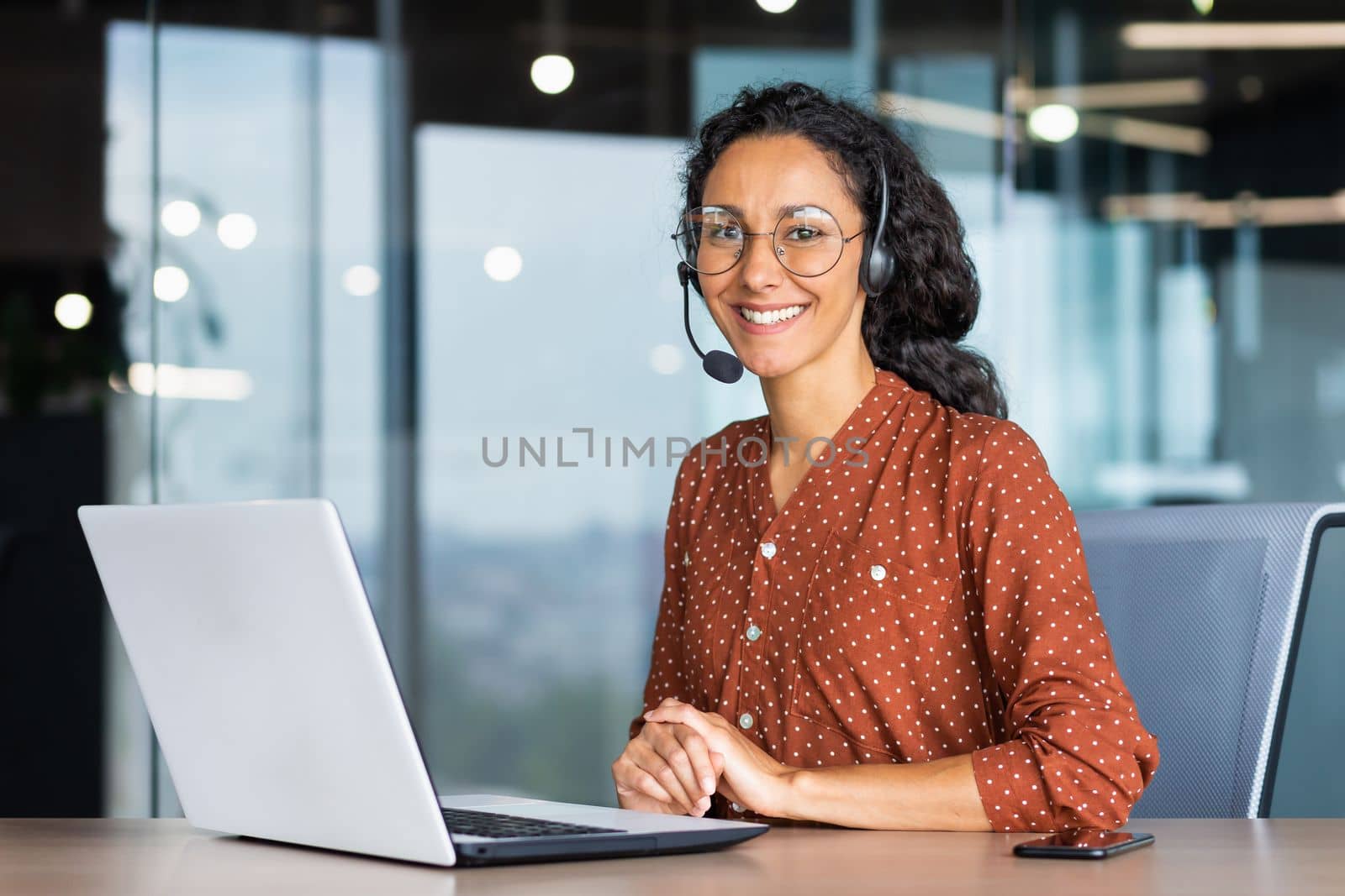 Portrait of Latin American business woman, office worker looking at camera and smiling, using headset and laptop for remote online communication, customer support tech call center worker.