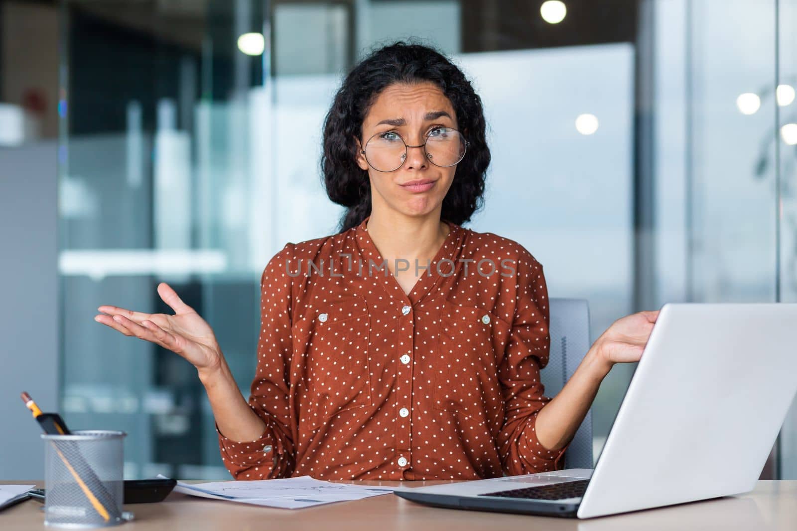 Frustrated and tired business woman looking at camera, Hispanic woman unhappy with work result, working inside office using laptop at work.