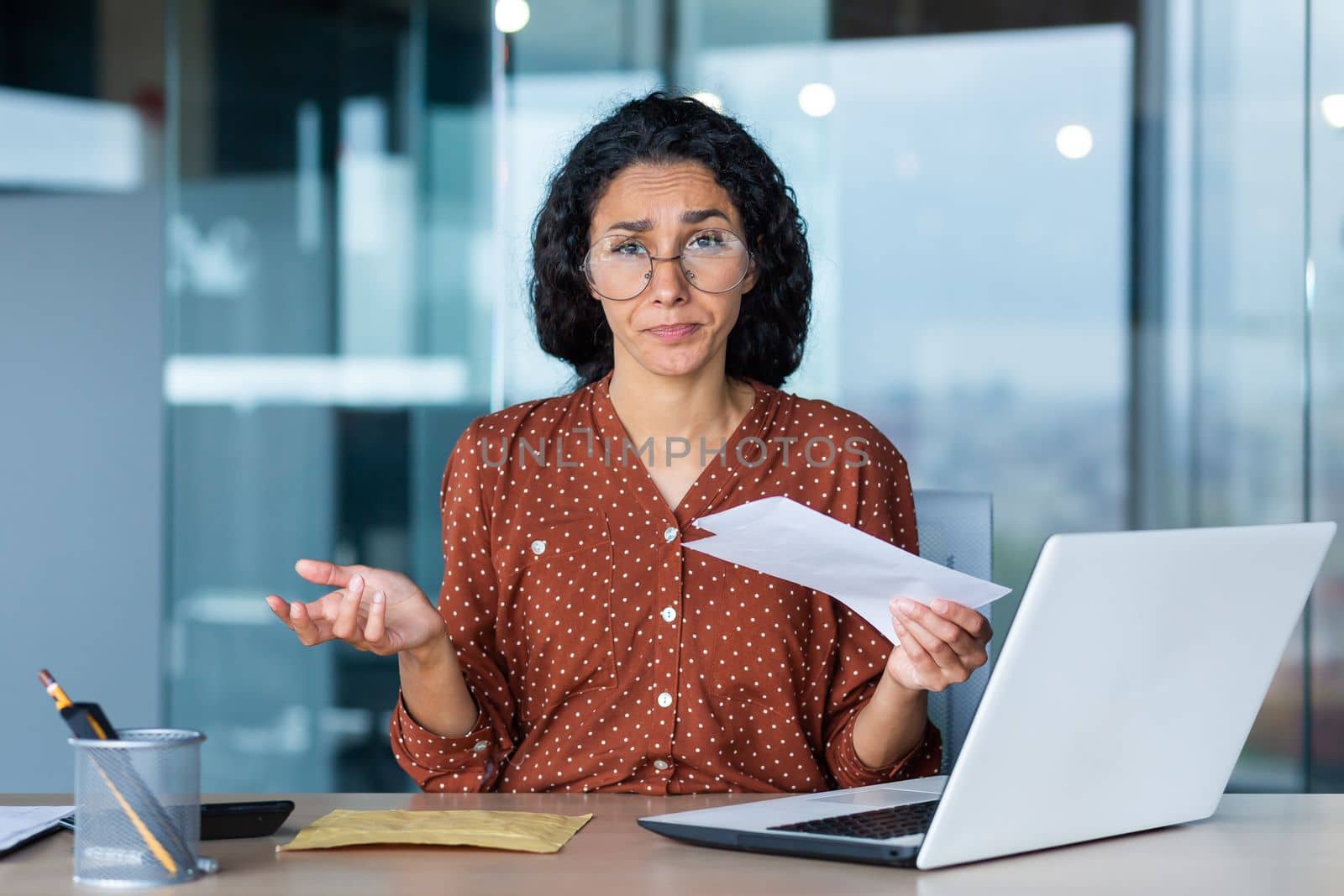 Portrait of disappointed business woman, latin american received notification letter from bank with bad news, office worker looking sad at camera, working at work using laptop.