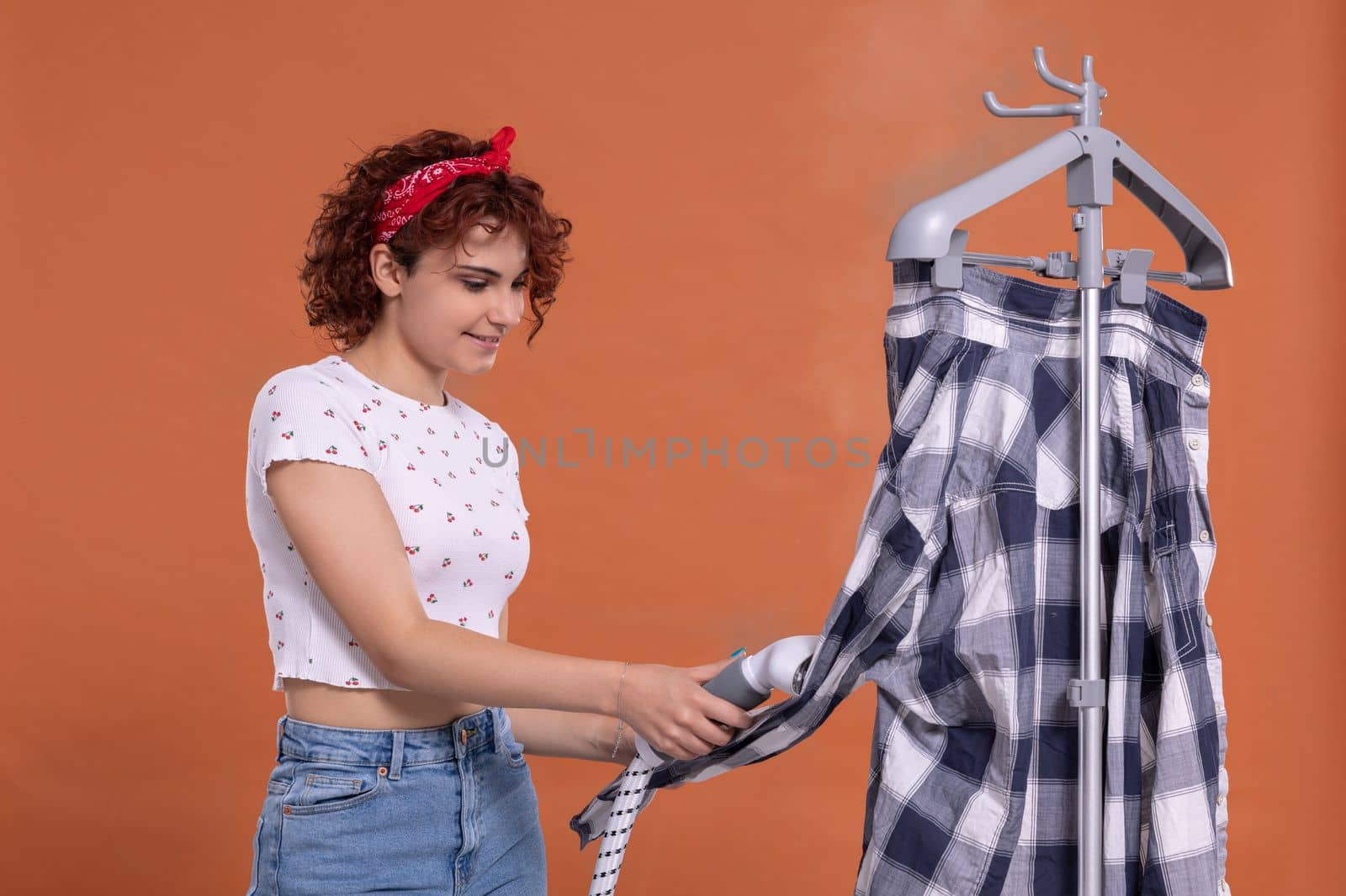 Smiling girl using a steamer to iron a man's shirt. Attractive girl with dark and curly hair. Hot steam.
