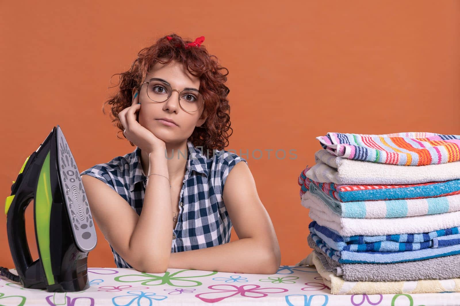 The girl, having finished her work, waits for the next one. The ironed towels lie on the ironing board. Isolated from the background.