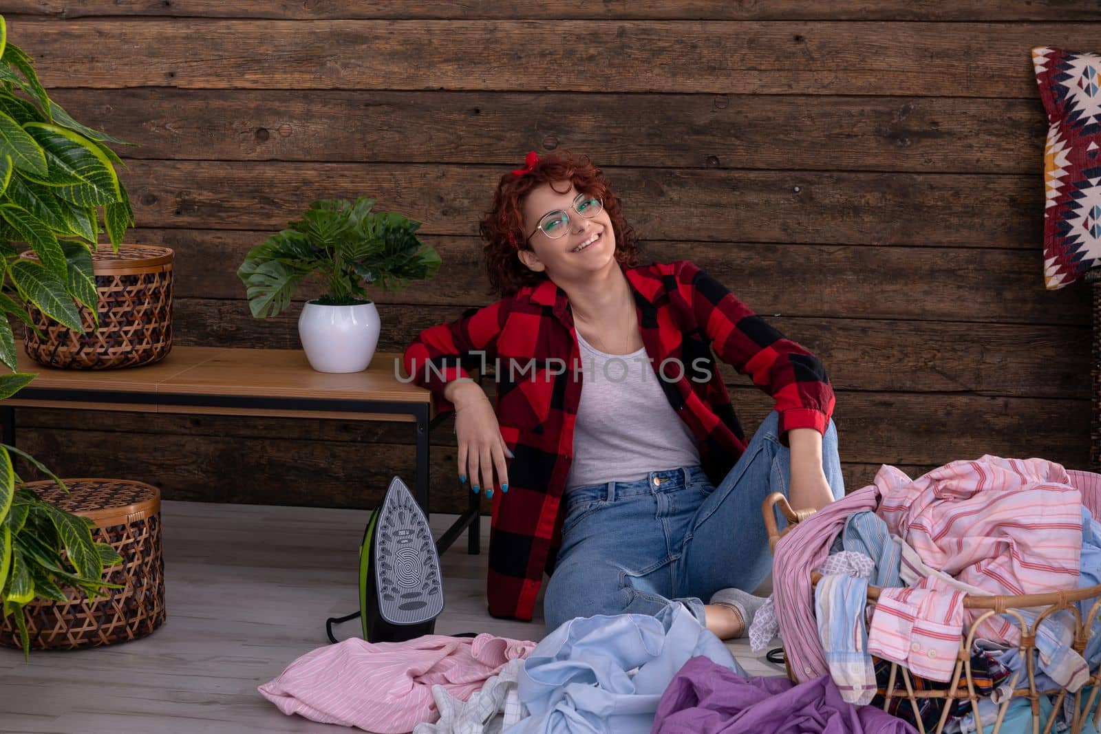Happy and smiling girl that she will be able to quickly iron clean clothes after washing. Full of vigor and strength to work. A wall in the house made of boards.