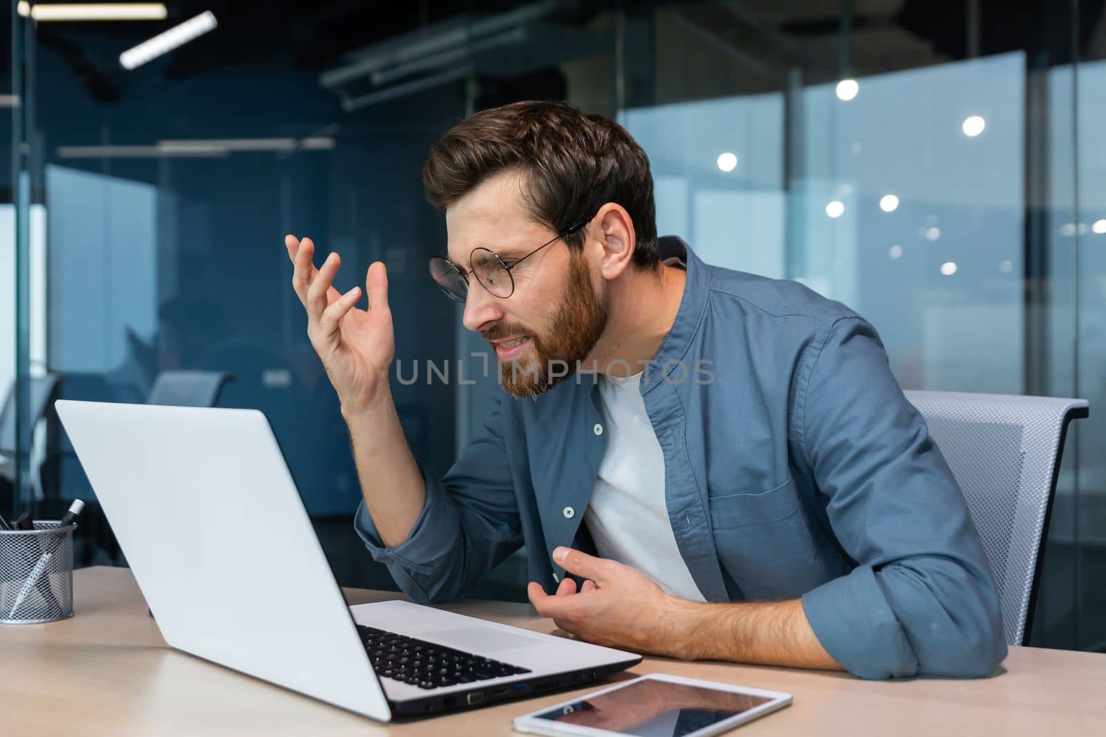 Dissatisfied and angry businessman looking at laptop screen, man in casual shirt working inside office annoyed employee.