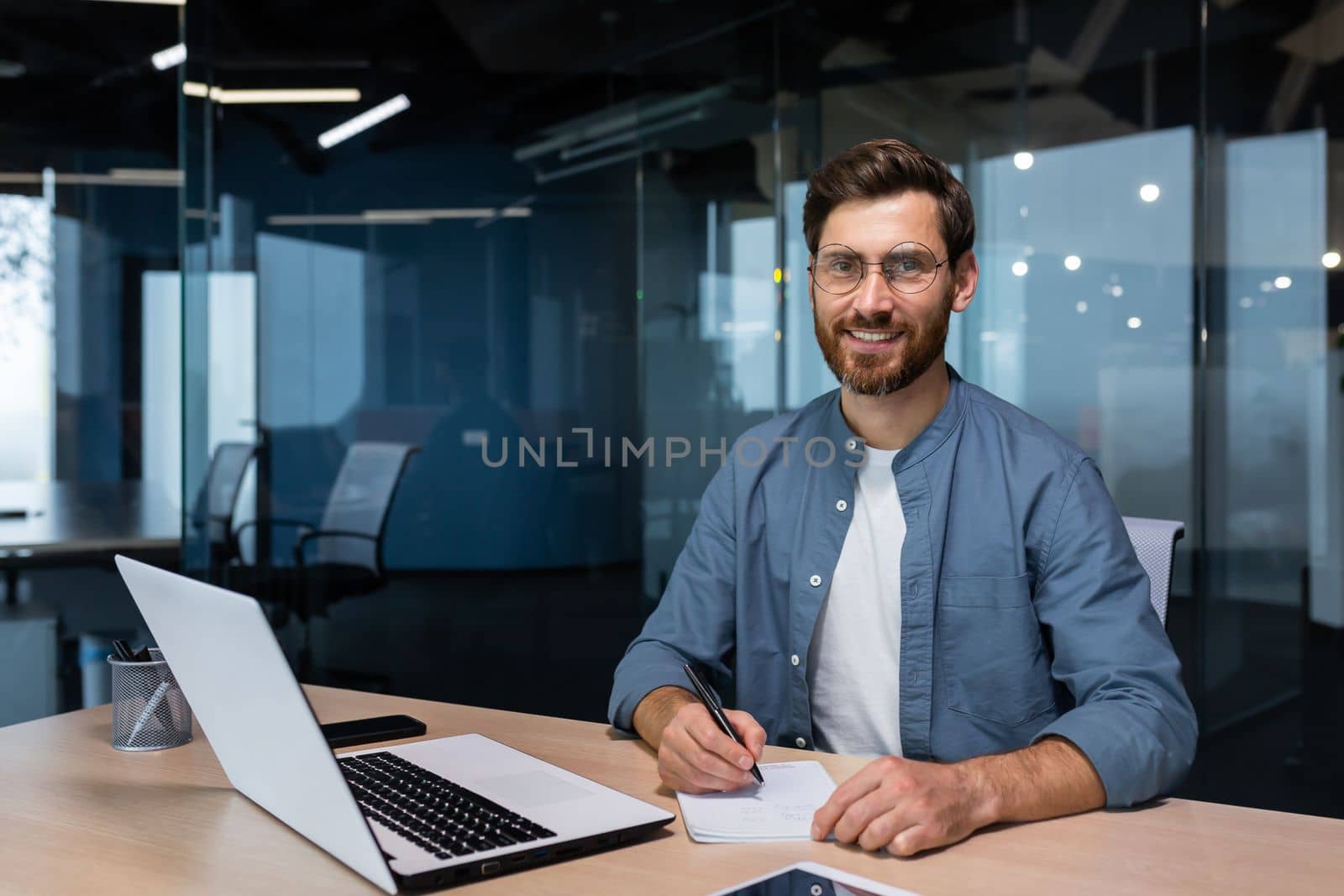 Portrait of successful businessman behind paper work, man in shirt smiling and looking at camera, financier boss inside office using laptop in work at workplace.
