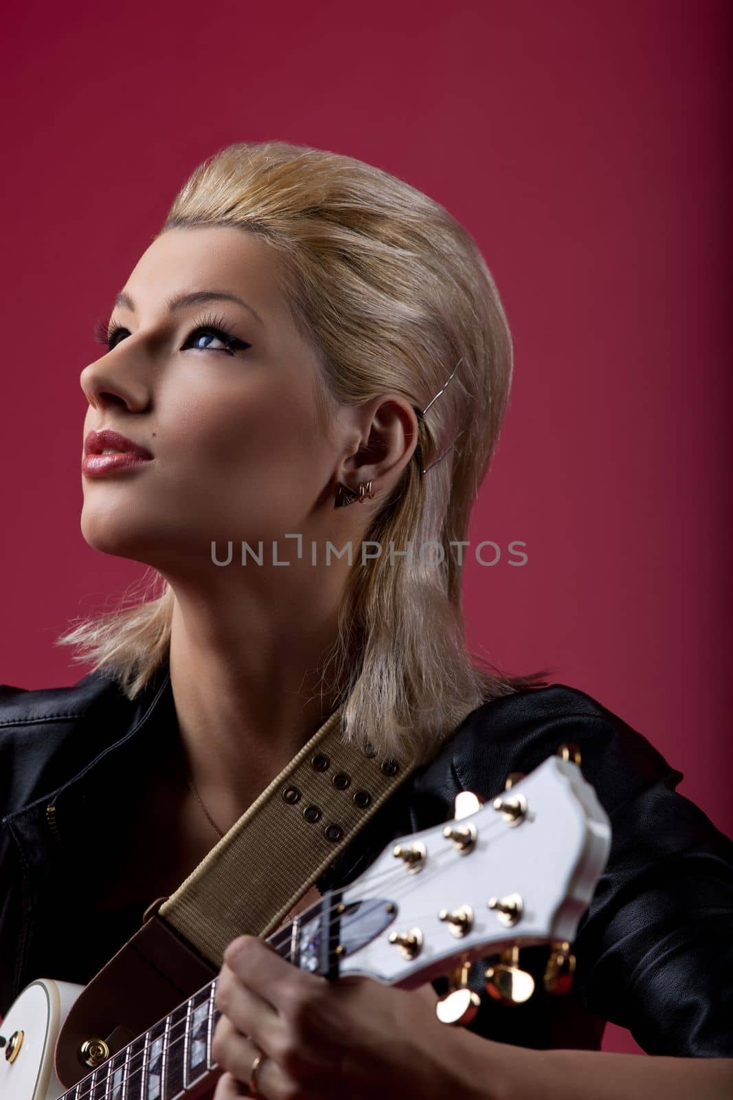 Sexy rock woman in black leather posing romantic with electro guitar on red background