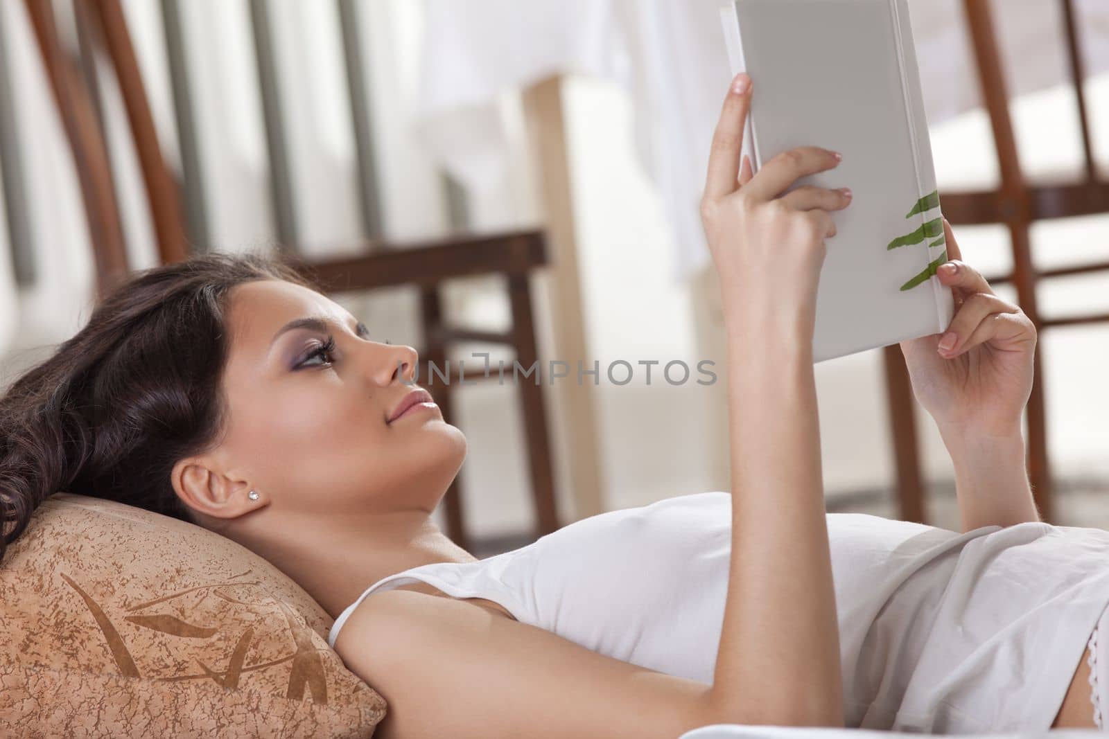 young woman lay in bed and read book in morning interior