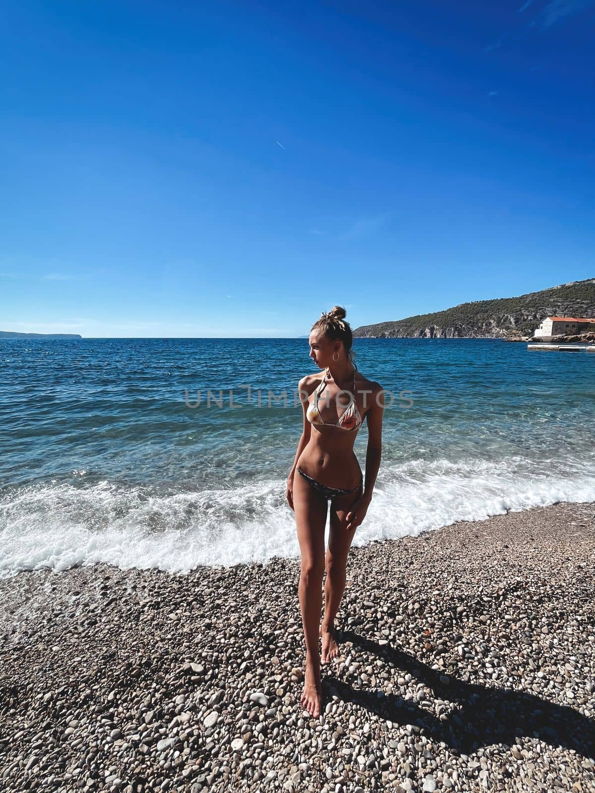 Beautiful tall model in a swimsuit on the rocky shore against the background of the sea and distant islands.