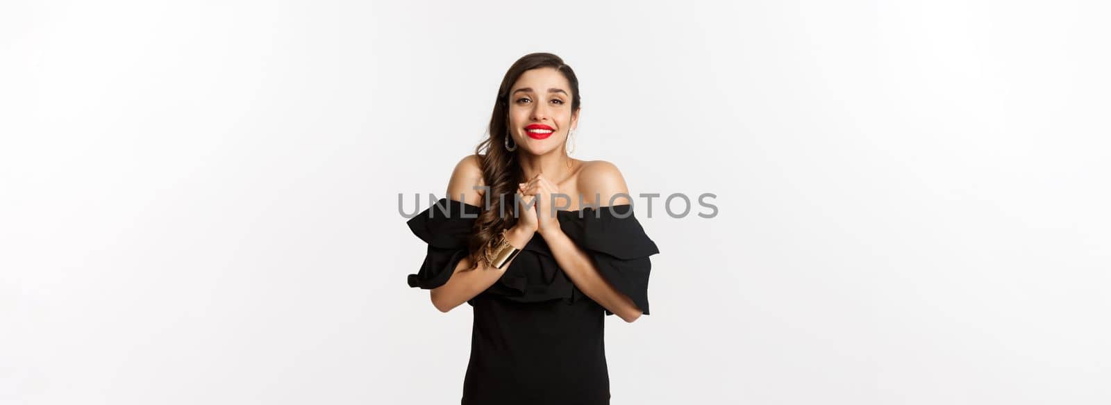 Fashion and beauty. Pretty woman in black dress asking for help, showing thank you gesture, looking grateful at camera, standing over white background by Benzoix