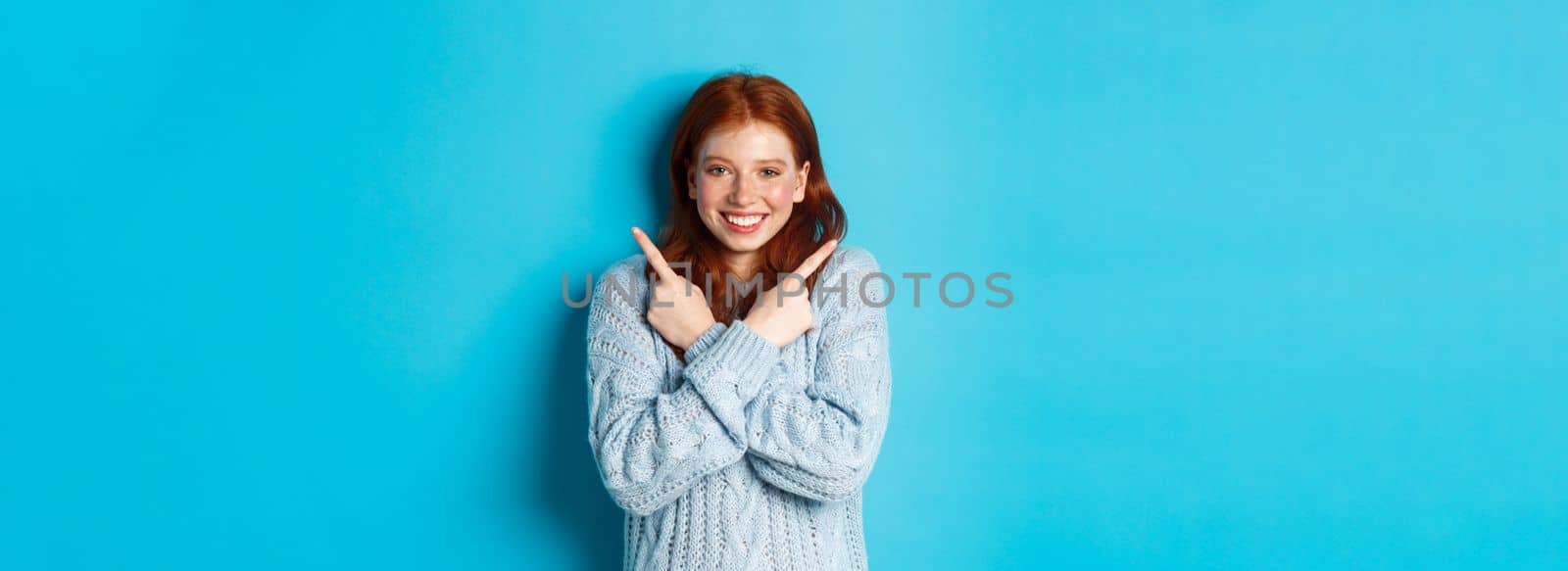 Cheerful redhead girl showing two choices, pointing sideways and smiling over blue background by Benzoix