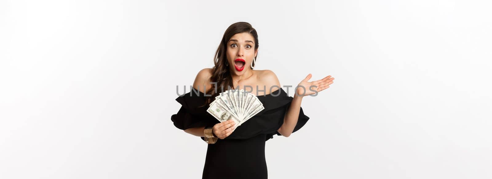 Beauty and shopping concept. Excited lucky woman winning money, looking amazed and holding dollars, standing over white background by Benzoix