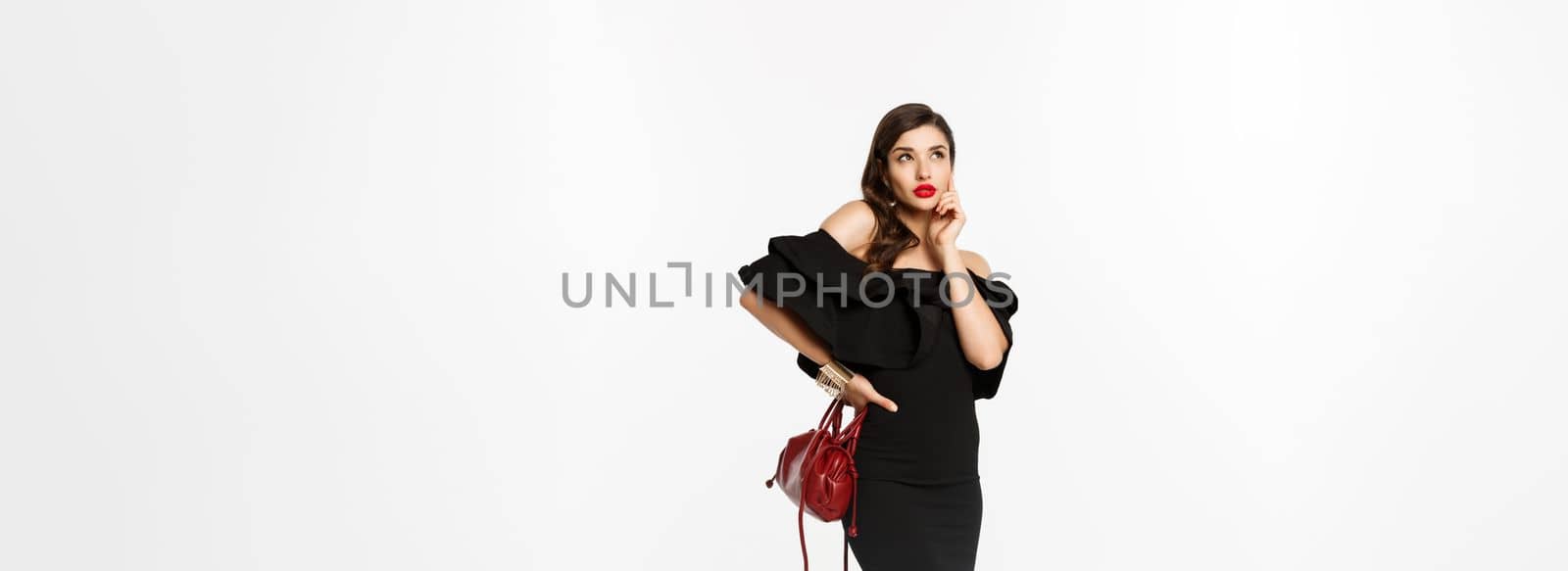 Beauty and fashion concept. Full length of beautiful and stylish woman in black dress thinking about shopping, looking at upper left corner, holding purse, white background by Benzoix