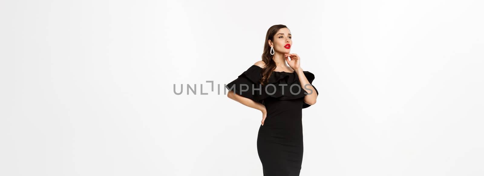 Vertical view of beautiful young woman in luxurious dress, red lips and jewelry, standing with christmas gifts on white background, standing over white background.