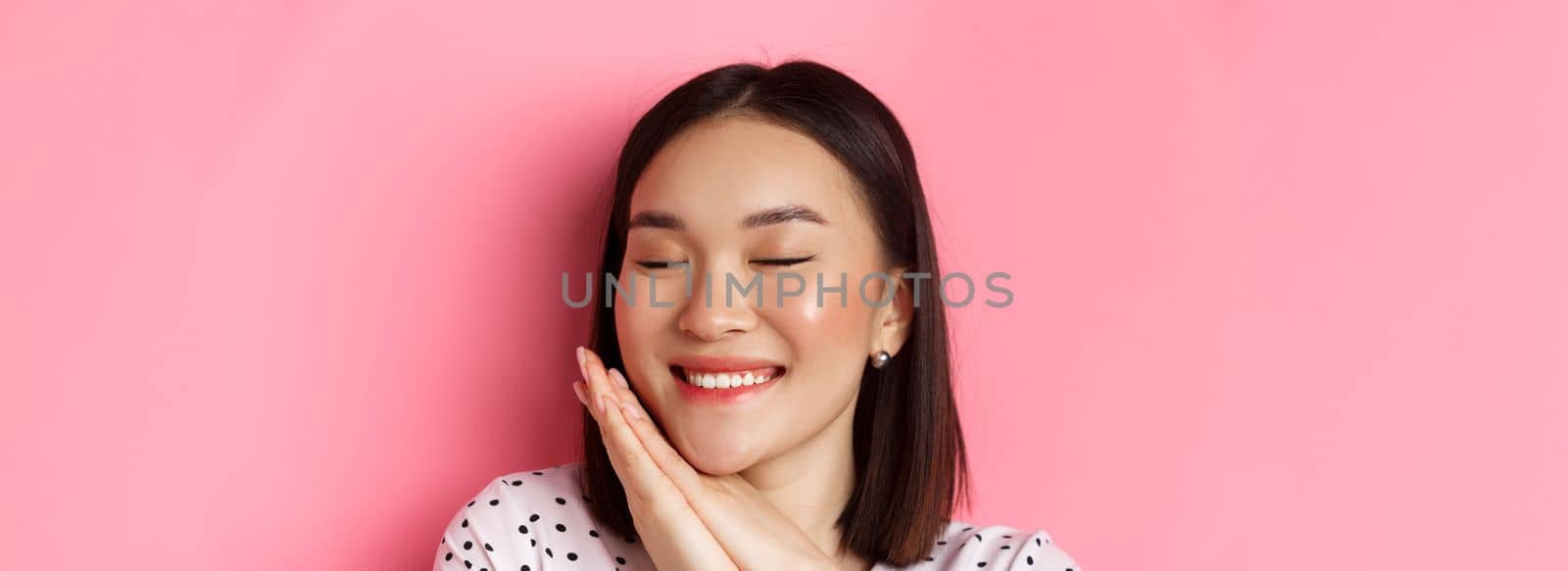 Beauty and skin care concept. Headshot of adorable and dreamy asian woman close eyes, smiling nostalgic, standing against pink background by Benzoix
