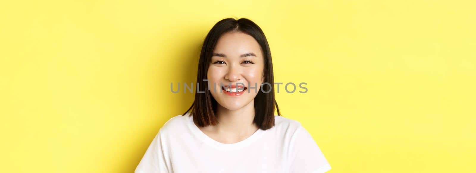 Beauty. Close up of smiling cute asian woman with perfect white smile teeth and glowing skin, standing over yellow background in t-shirt by Benzoix