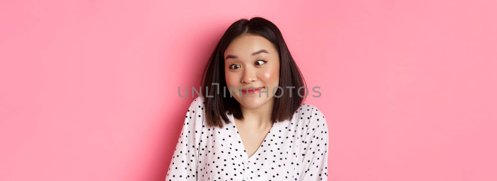 Beauty and lifestyle concept. Close-up of funny and cute asian woman squinting eyes and smiling, fool around at camera, standing over pink background by Benzoix
