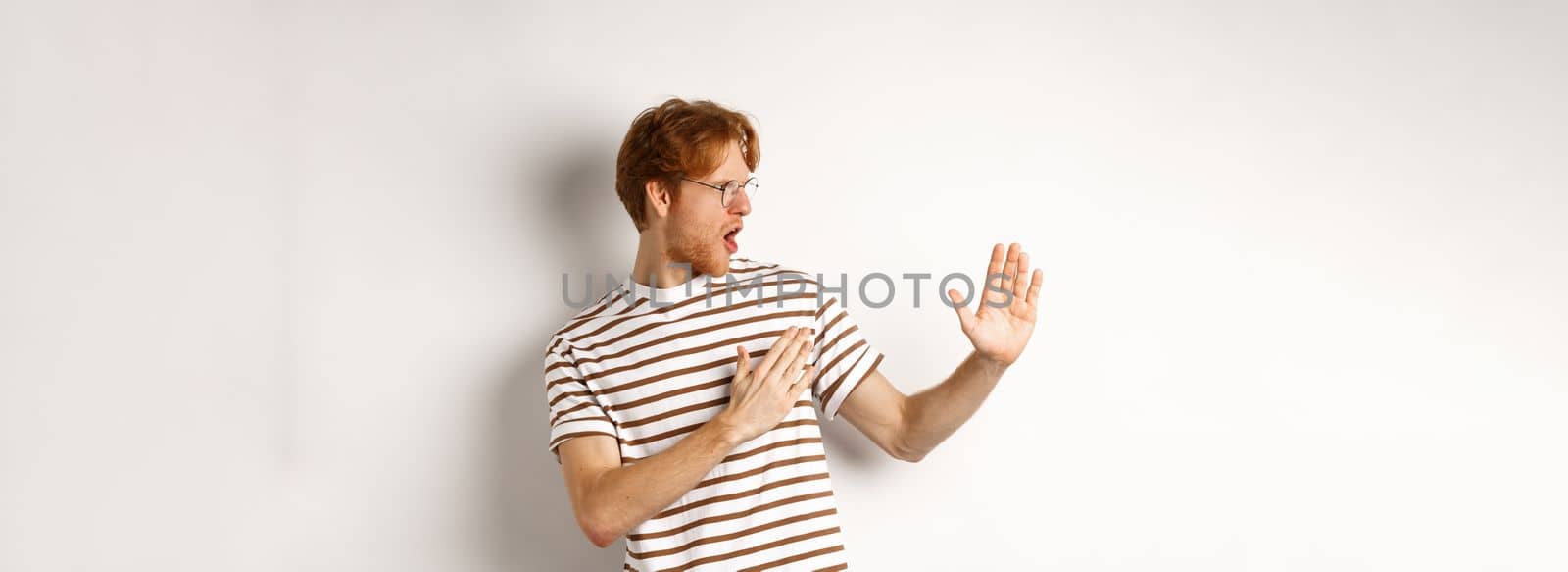 Funny redhead man standing in martial arts pose, fighting shadow and looking left, standing over white background.
