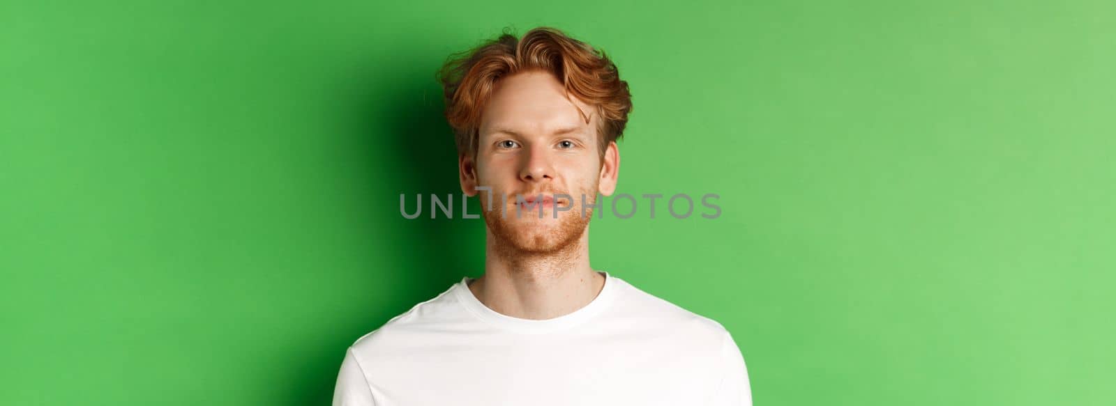 Close-up of young man with red messy hair and beard looking at camera, standing over green background by Benzoix