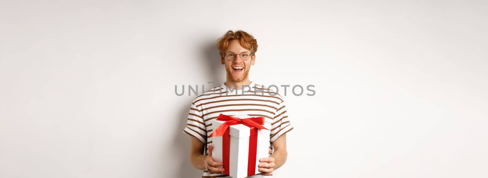 Valentines day and holidays concept. Cheerful young man holding gift box and smiling grateful, receiving presents, standing over white background by Benzoix