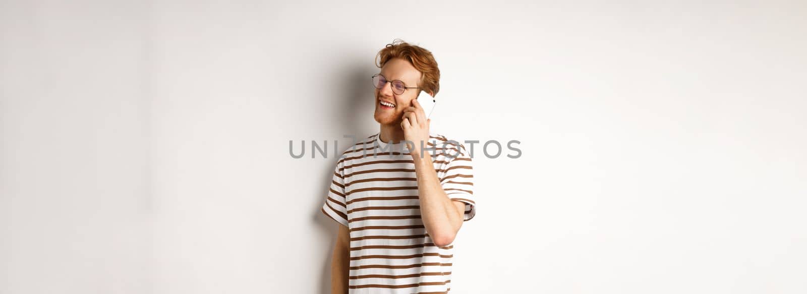 Profile of happy young handsome man talking on mobile phone, looking left and smiling, standing over white background.