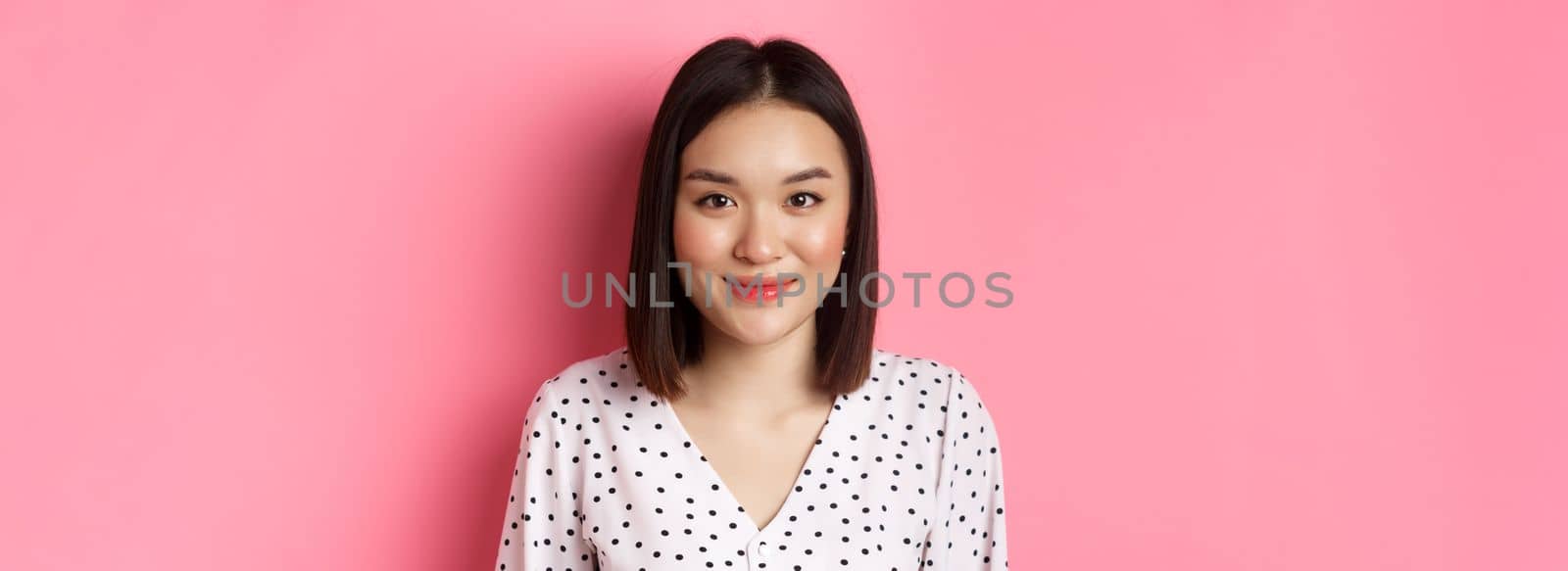 Close-up of cute asian female model looking at camera, blushing and smiling kawaii, standing over pink background by Benzoix
