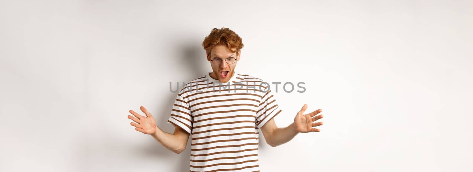 Impressed redhead man in glasses showing length of something big, demonstrate large size and looking amazed, standing over white background.