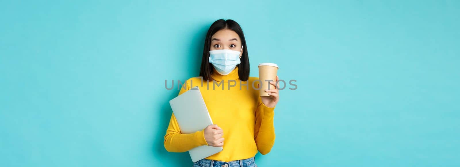 covid-19, health care and quarantine concept. Asian girl student in medical mask standing with laptop and coffee from cafe, standing over blue background by Benzoix