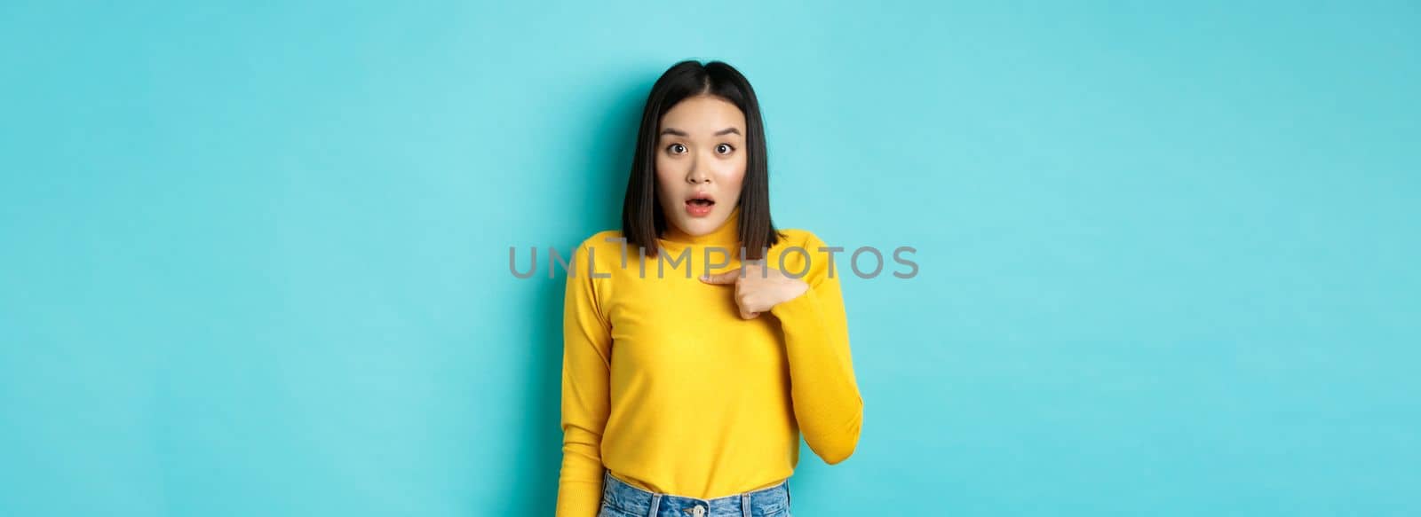 Image of surprised asian girl gasping and pointing at herself with disbelief, standing over blue background by Benzoix