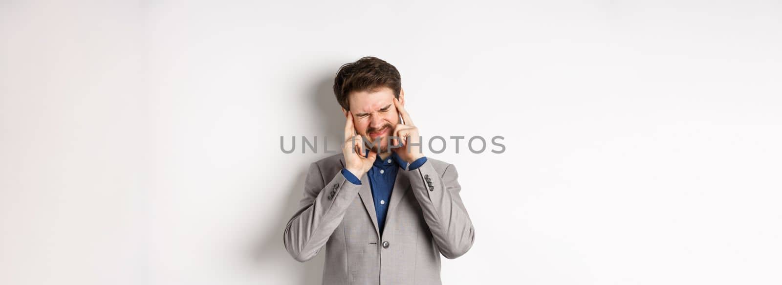 Business man in suit having headache, grimacing and touching head, suffer migraine, standing sick on white background.