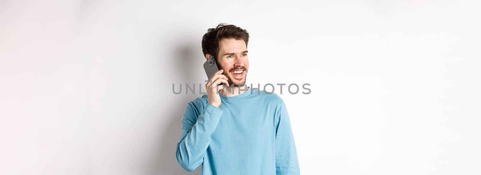 Technology concept. Joyful man enjoying phone call, talking on smartphone and smiling, standing in casual shirt over white background by Benzoix