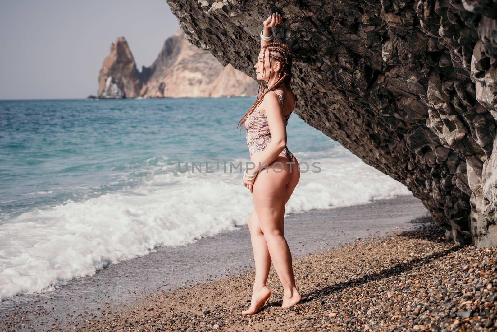 Beach vacation. Hot beautiful woman in sunhat and bikini standing with her arms raised to her head enjoying looking view of beach ocean on hot summer day.