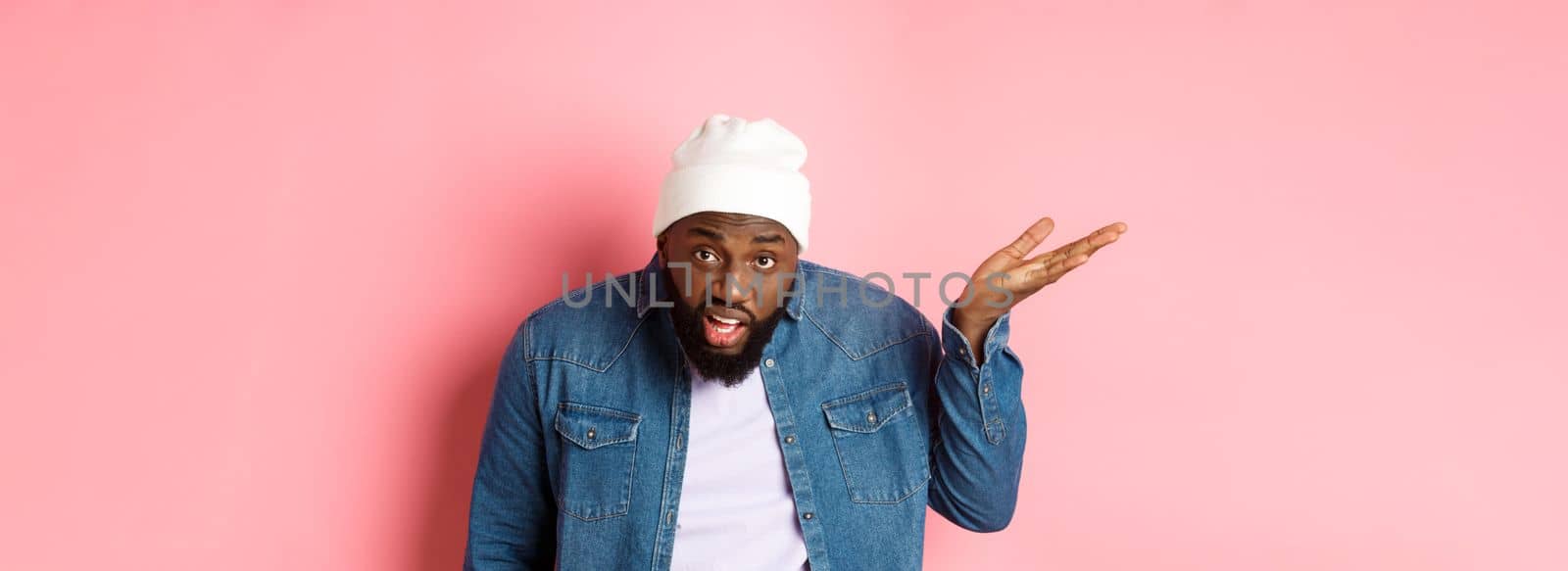 Annoyed and pissed-off Black man arguing, staring at camera and scolding person, standing over pink background.