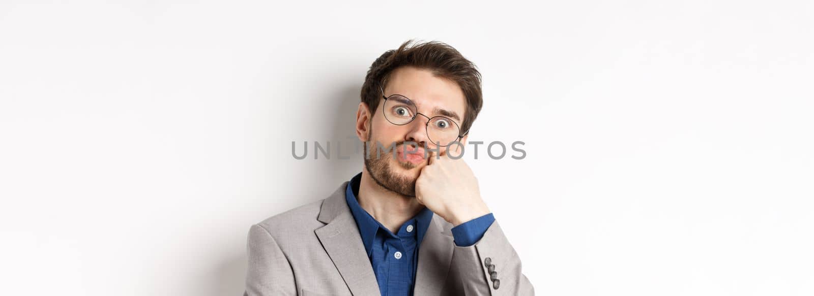 Bored funny office worker in glasses, pouting and holding breath, staring with popped eyes at camera, white background.