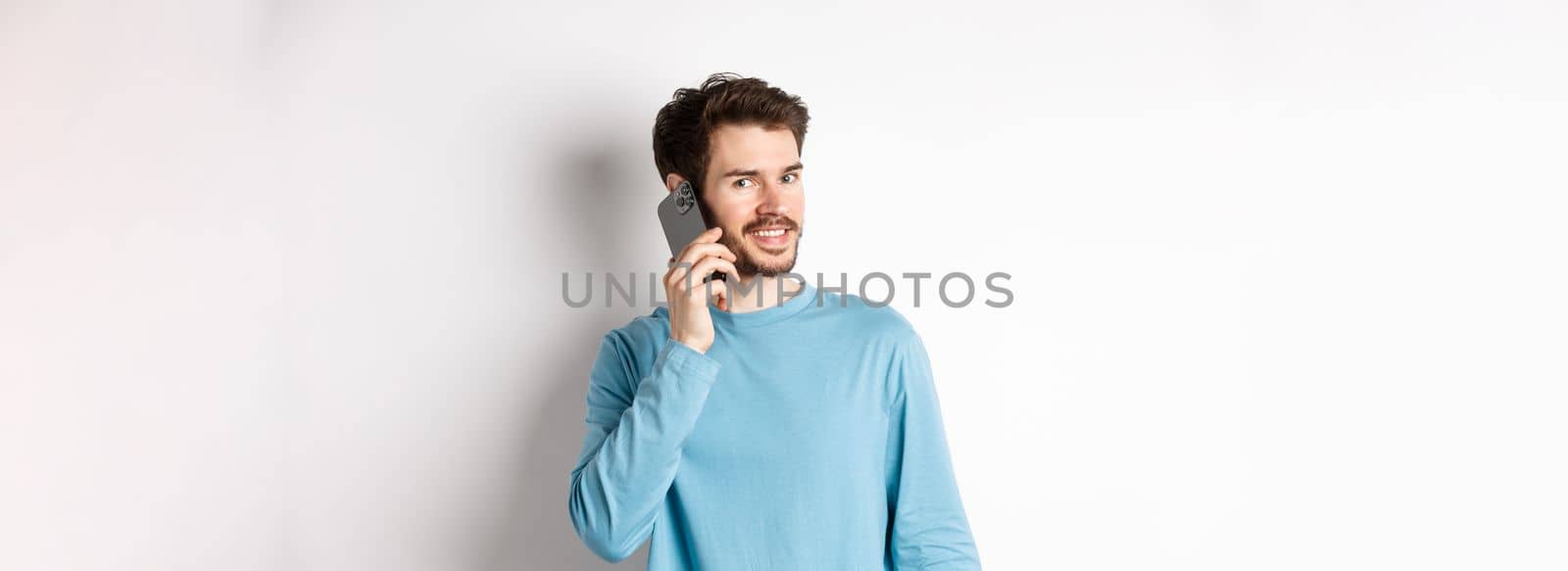 Technology concept. Young male model talking on mobile phone, calling someone on smartphone and smiling, standing over white background by Benzoix