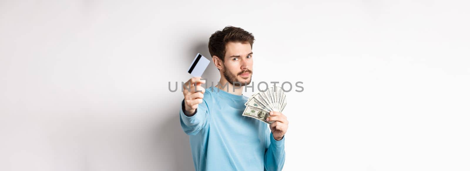 Serious-looking guy stretch out hand with plastic credit card, prefer contactless payment instead of cash, standing on white background.