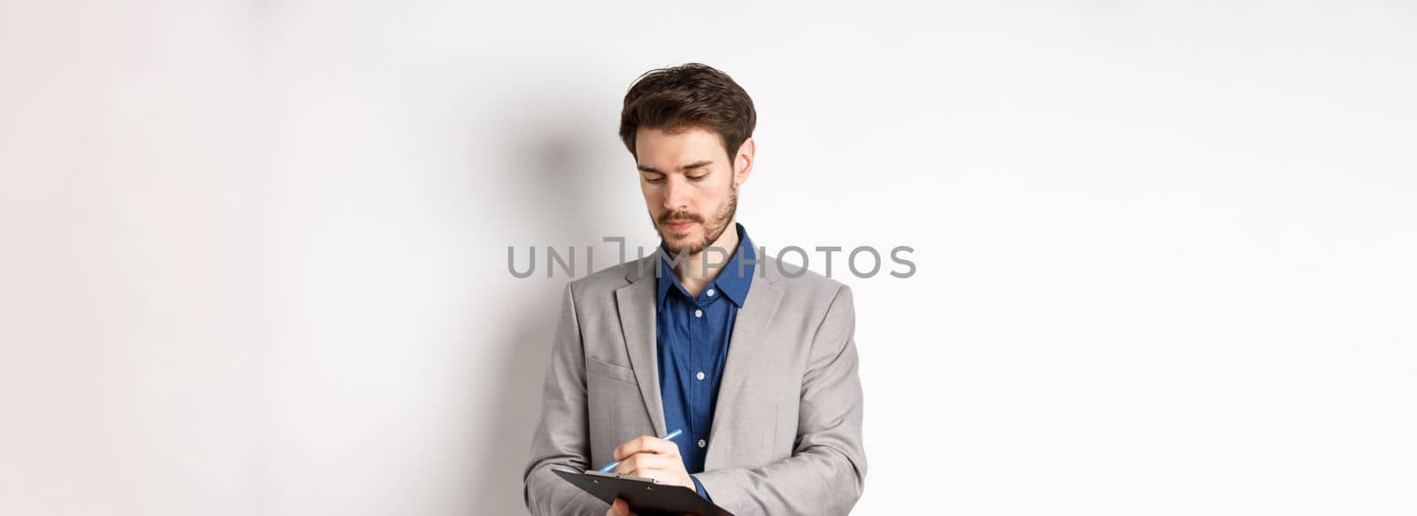 Office worker in suit writing on clipboard, taking notes on meeting, standing on white background.