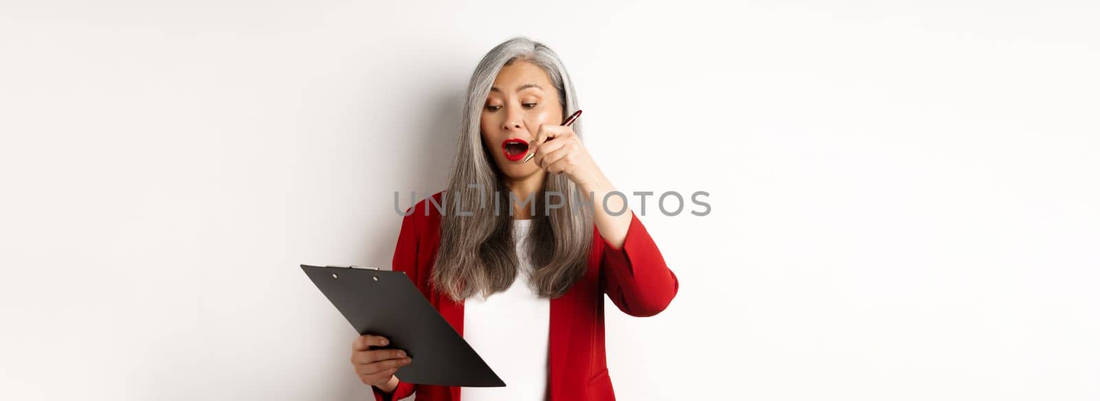 Successful asian female entrepreneur taking notes on clipboard, working on report and looking excited, standing over white background.