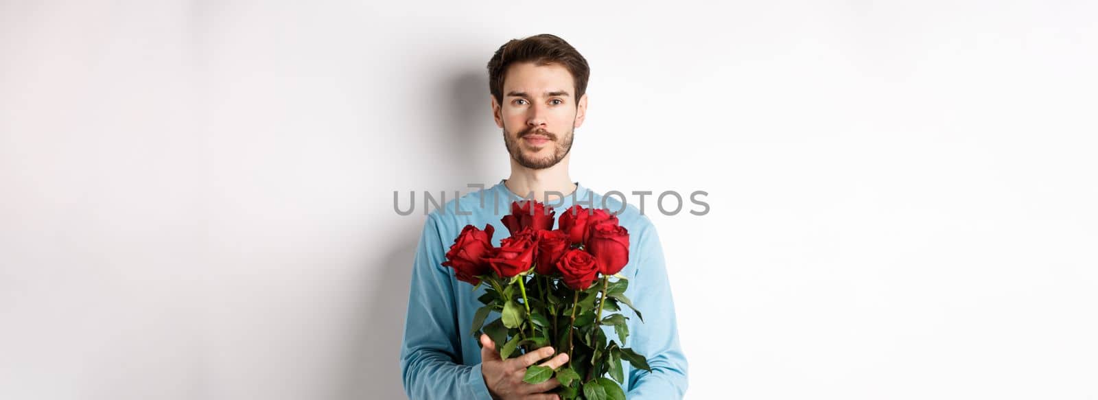 Confident young man bring flowers on Valentines day date, holding romantic bouquet, standing over white background by Benzoix