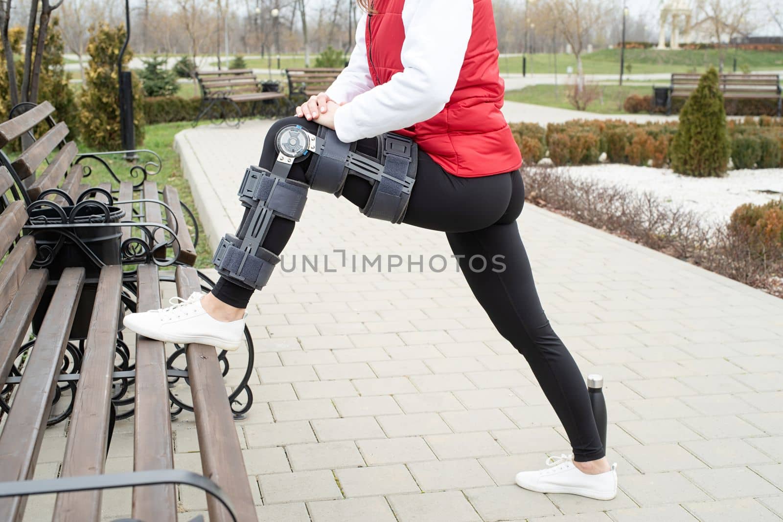 Woman wearing sport clothes and knee brace or orthosis after leg surgery, walking down the stairs in the park. Medical and healthcare concept.