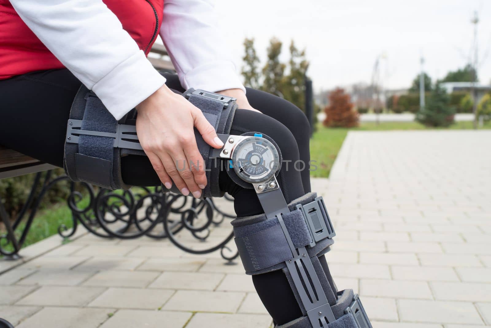 Woman wearing knee brace or orthosis after leg surgery, walking in the park by Desperada