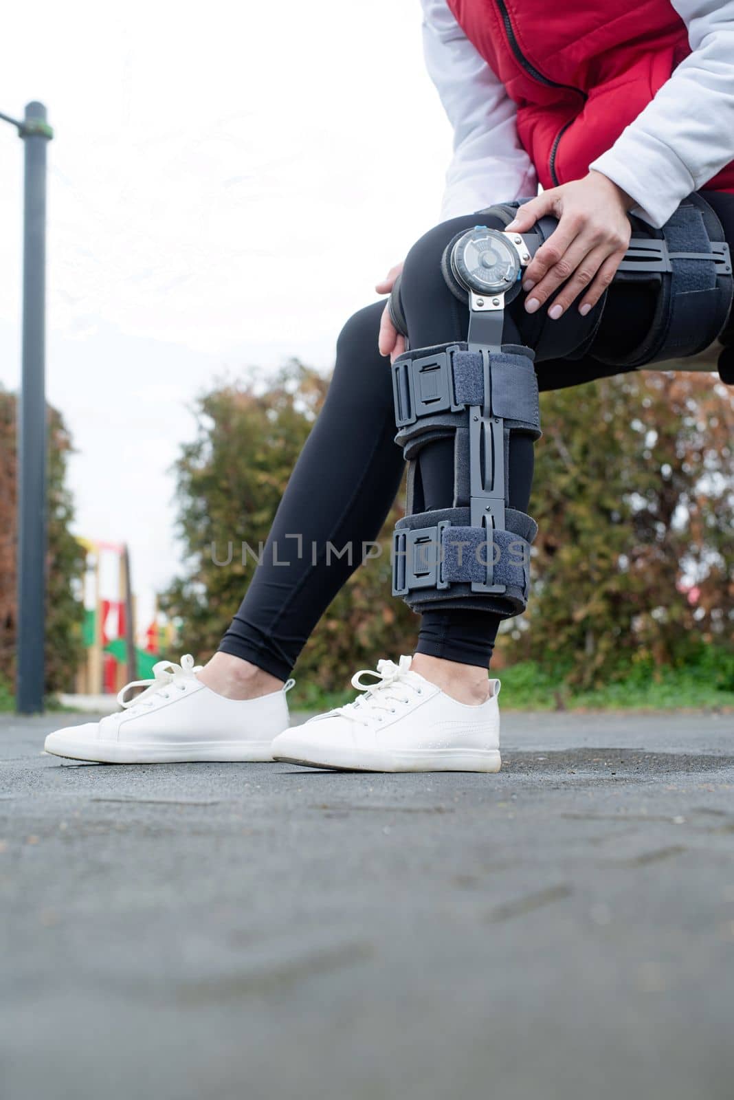 Woman wearing sport clothes and knee brace or orthosis after leg surgery, walking down the stairs in the park. Medical and healthcare concept.