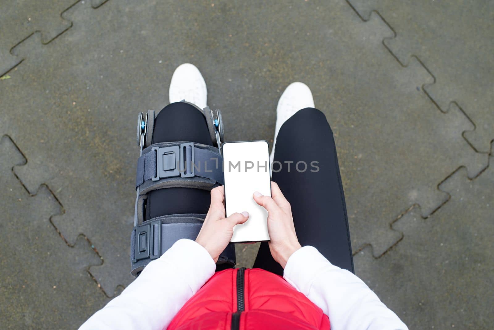 Woman wearing sport clothes and knee brace or orthosis after leg surgery, walking down the stairs in the park. Medical and healthcare concept.